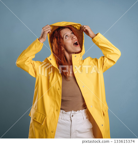 Looking for a rain, in yellow coat. Woman is in the studio against background Looking for a rain, in yellow coat. Woman is in the studio against background 133615374