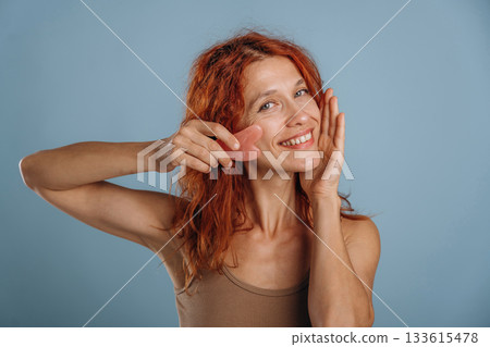 Pink colored face patch being used on the skin. Woman is in the studio against background 133615478