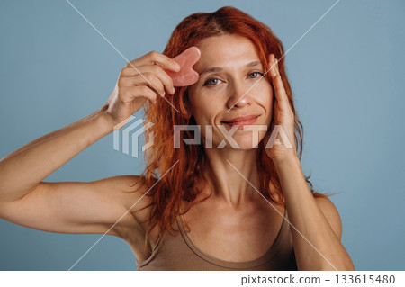 Pink colored face patch being used on the skin. Woman is in the studio against background Pink colored face patch being used on the skin. Woman is in the studio against background 133615480