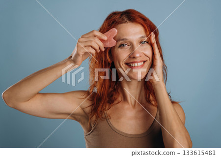 Pink colored face patch being used on the skin. Woman is in the studio against background Pink colored face patch being used on the skin. Woman is in the studio against background 133615481