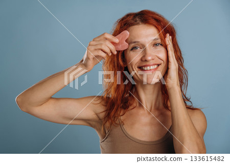 Pink colored face patch being used on the skin. Woman is in the studio against background 133615482