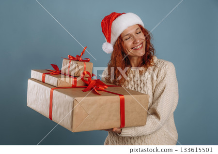 Boxes with presents in hands, in Santa hat. Woman is in the studio against background Boxes with presents in hands, in Santa hat. Woman is in the studio against background 133615501