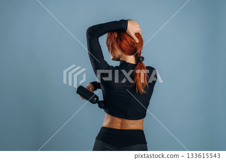 Process of using electric massager, in sportive fitness clothes. Woman is in the studio against background Process of using electric massager, in sportive fitness clothes. Woman is in the studio against background 133615543