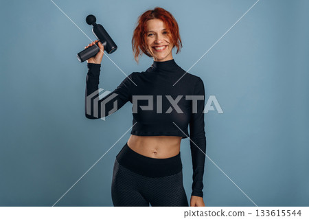 Process of using electric massager, in sportive fitness clothes. Woman is in the studio against background Process of using electric massager, in sportive fitness clothes. Woman is in the studio against background 133615544