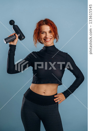 Process of using electric massager, in sportive fitness clothes. Woman is in the studio against background Process of using electric massager, in sportive fitness clothes. Woman is in the studio against background 133615545