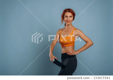 Automatic massager is being used. In sport clothes. Woman is in the studio against background Automatic massager is being used. In sport clothes. Woman is in the studio against background 133615561