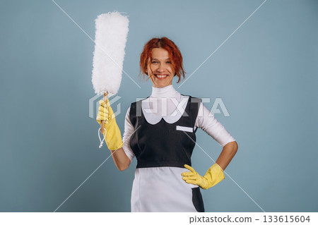 Ready to clean some dust. Maid in uniform. Woman is in the studio against background Ready to clean some dust. Maid in uniform. Woman is in the studio against background 133615604