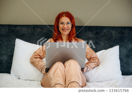 Using laptop, in pajama, on the bed. Woman is in the hotel room, modern interior 133615766