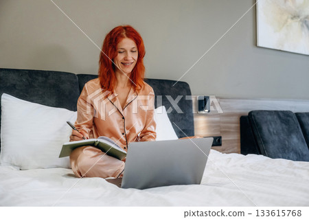 Using laptop, in pajama, on the bed. Woman is in the hotel room, modern interior 133615768