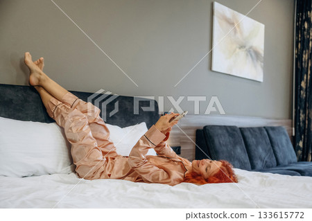 Smartphone in hands, lying down on the bed. Woman is in the hotel room, modern interior Smartphone in hands, lying down on the bed. Woman is in the hotel room, modern interior 133615772