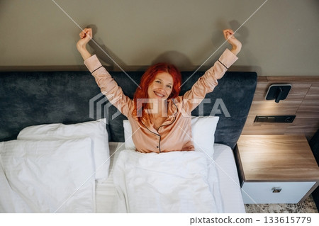 Just woke up, with hands up, on the bed in pajama. Woman is in the hotel room, modern interior Just woke up, with hands up, on the bed in pajama. Woman is in the hotel room, modern interior 133615779