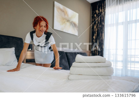 Front view, preparing the bed. Maid is working in modern hotel room 133615796