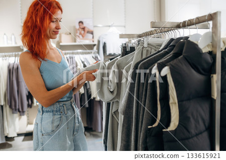 Redhead woman chooses clothes in retail store Redhead woman chooses clothes in retail store 133615921