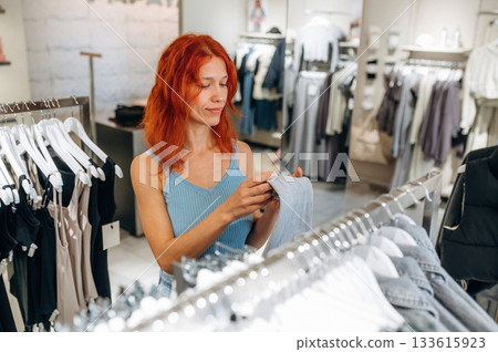 Redhead woman chooses clothes in retail store Redhead woman chooses clothes in retail store 133615923