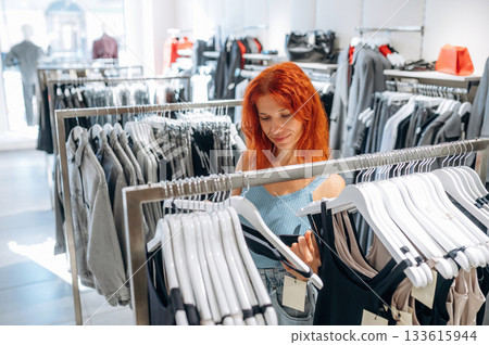 In blue dress, redhead. Woman chooses clothes in retail store In blue dress, redhead. Woman chooses clothes in retail store 133615944