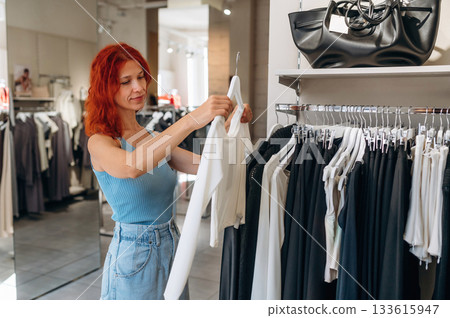 In blue dress, redhead. Woman chooses clothes in retail store 133615947
