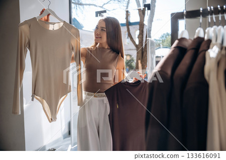 Brunette woman chooses clothes in retail store Brunette woman chooses clothes in retail store 133616091