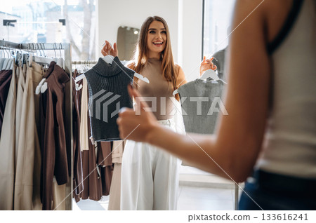 Showing thumb up. Two female friends are in the retail store, choosing clothes, shopping 133616241