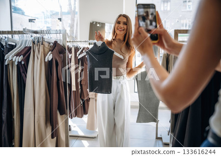 Making a photo by using smartphone. Two female friends are in the retail store, choosing clothes, shopping 133616244