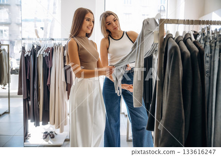 Checking the sweater. Two female friends are in the retail store, choosing clothes, shopping Checking the sweater. Two female friends are in the retail store, choosing clothes, shopping 133616247