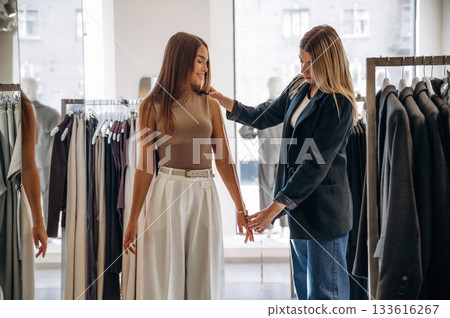 Standing and measuring the hand length. Two female friends are in the retail store, choosing clothes, shopping 133616267