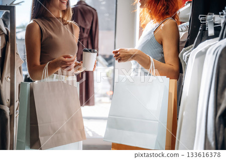 Casual conversation, with drink. Two female friends are in the retail store, choosing clothes, shopping Casual conversation, with drink. Two female friends are in the retail store, choosing clothes, shopping 133616378