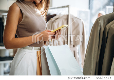 Smartphone in hands. Close up view of woman that is chooses clothes in the retail shop Smartphone in hands. Close up view of woman that is chooses clothes in the retail shop 133616673