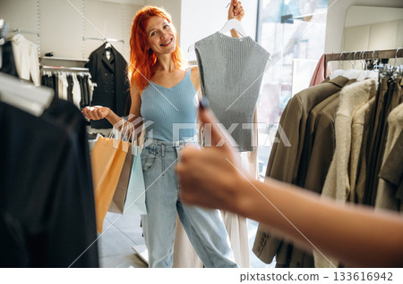 Showing thumb up. Two female friends are in the retail store, choosing clothes, shopping Showing thumb up. Two female friends are in the retail store, choosing clothes, shopping 133616942