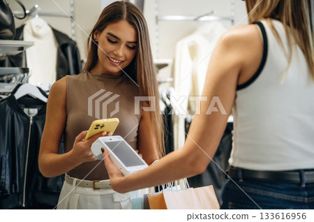 Worker is holding the terminal. Woman is paying for clothes, in the retail store Worker is holding the terminal. Woman is paying for clothes, in the retail store 133616956