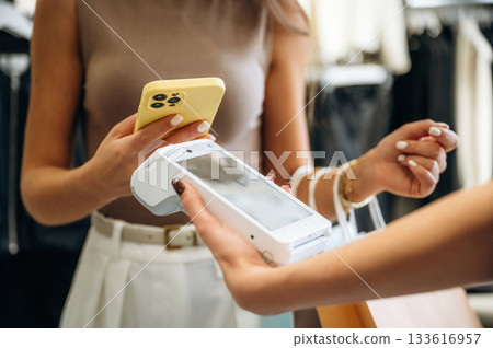 Worker is holding the terminal. Woman is paying for clothes, in the retail store Worker is holding the terminal. Woman is paying for clothes, in the retail store 133616957