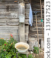 Rustic outdoor washing area with metal basins, wooden wall, garden tools, and blooming flowers. 133617523