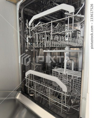 Open empty dishwasher with clean metal racks in a modern kitchen setting. Home Cleaning Routine 133617526