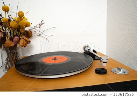 Vinyl record resting on a turntable in a home interior. Simple everyday music scene showing casual listening setup. Concept of music, audio, analog, home, lifestyle, leisure. Vinyl record resting on a turntable in a home interior. Simple everyday music scene showing casual listening setup. Concept of music, audio, analog, home, lifestyle, leisure. 133617556