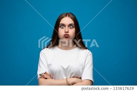 Expressive young woman posing with a confused facial expression against a bright blue studio background 133617629