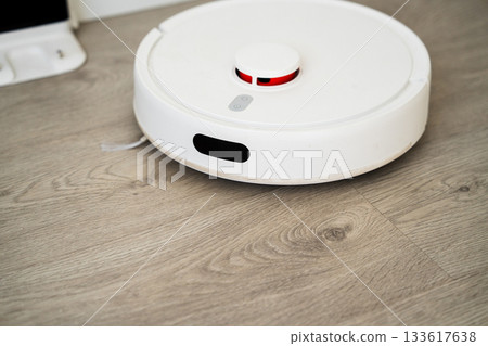 Front view of smart robotic vacuum cleaner on wooden floor performing automated home cleaning task Front view of smart robotic vacuum cleaner on wooden floor performing automated home cleaning task 133617638