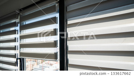 Striped zebra roller blinds on large windows providing adjustable light control in modern bright interior 133617662