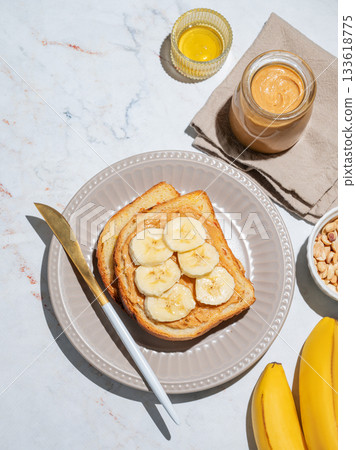 Peanut butter toast and banana on a plate on a marble background with fruits 133618775