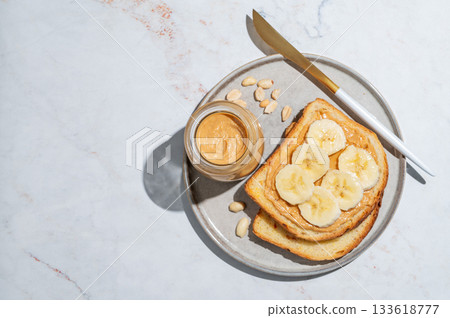 Peanut butter toast and banana on a plate on a marble background with nuts Peanut butter toast and banana on a plate on a marble background with nuts 133618777