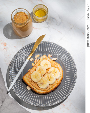 Peanut butter toast and banana on a dark plate on a marble background with honey 133618778