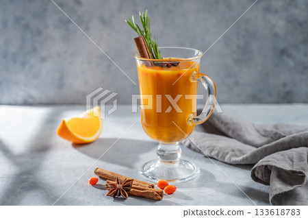 Sea buckthorn herbal tea in a glass on a blue background with orange, spices, and shadow. 133618783