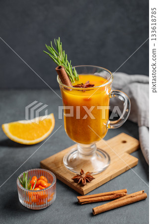 Sea buckthorn herbal tea in a glass on a wooden board on a dark background with orange, 133618785