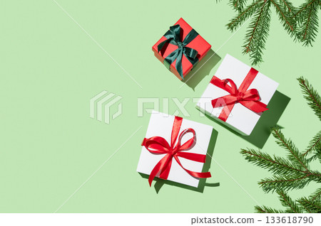 Several gift boxes with ribbons and fir branches on a green background Several gift boxes with ribbons and fir branches on a green background 133618790