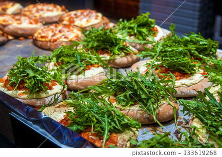 Freshly prepared flatbread with melted cheese and generous arugula topping displayed at a festive winter market food stall 133619268