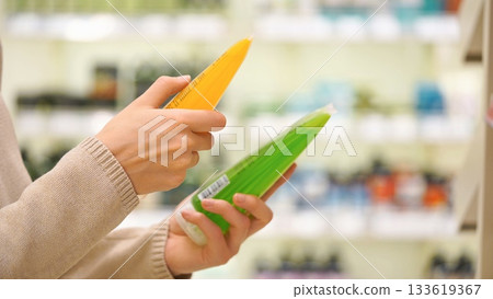 Woman comparing body wash or shower gel in a store aisle, reading cosmetic labels and ingredients to choose the best skincare product. 133619367