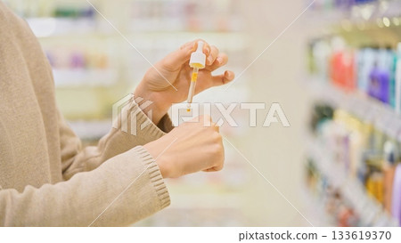 Woman testing serum texture on her hand before purchase in a beauty store, making an informed choice while selecting a cosmetic product for skincare. Woman testing serum texture on her hand before purchase in a beauty store, making an informed choice while selecting a cosmetic product for skincare. 133619370