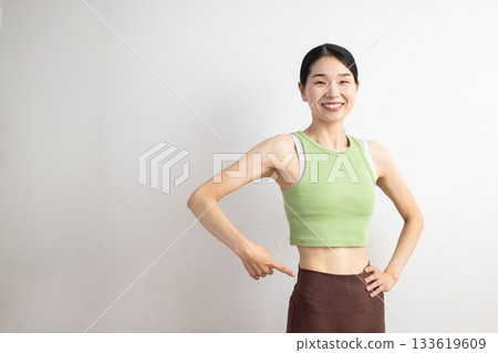 一位身穿瑜珈服的微笑女子指著自己的腰部 133619609