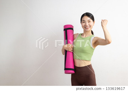 A smiling middle-aged woman holding a yoga mat and making a fist pump A smiling middle-aged woman holding a yoga mat and making a fist pump 133619617