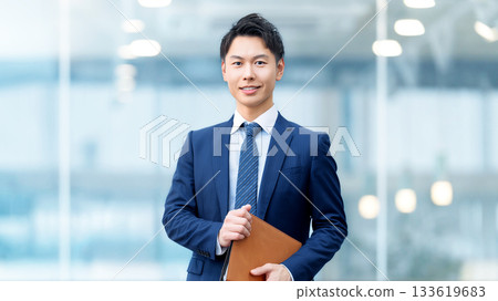Smiling male businessman holding a binder 133619683