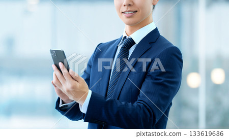 拿著智慧型手機的微笑的男性商人 拿著智慧型手機的微笑的男性商人 133619686