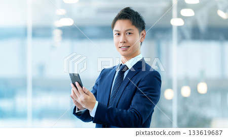 拿著智慧型手機的微笑的男性商人 拿著智慧型手機的微笑的男性商人 133619687